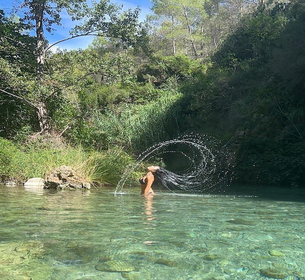 A person in a natural setting with clear water, surrounded by greenery and trees. 1