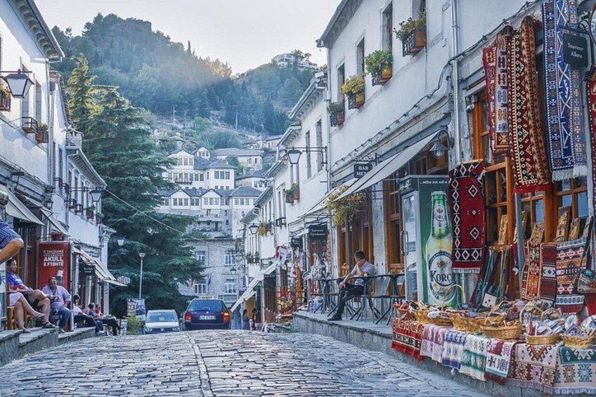 A cobblestone street in a town with buildings on either side, a car in the distance, and a person riding a bicycle. 3
