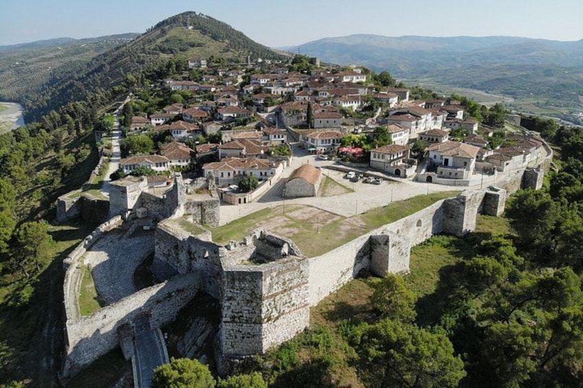 A historic town with a fortified castle, surrounded by lush greenery and a mountainous backdrop. 1