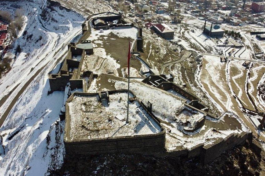 A snow-covered fortification with a flagpole, surrounded by snowdrifts and a river. 4