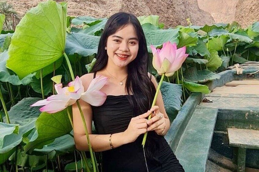 A person holding lotus flowers in a garden with large green leaves. 1