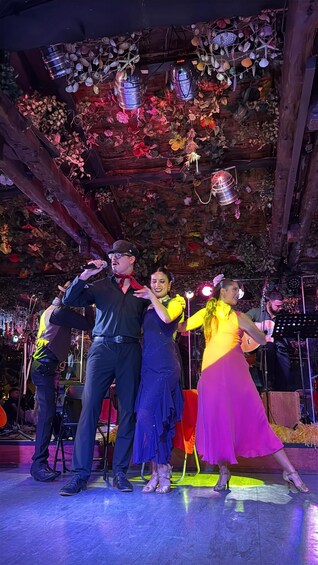 A group of people dancing on a stage with a wooden ceiling decorated with hanging lights and flowers. 4