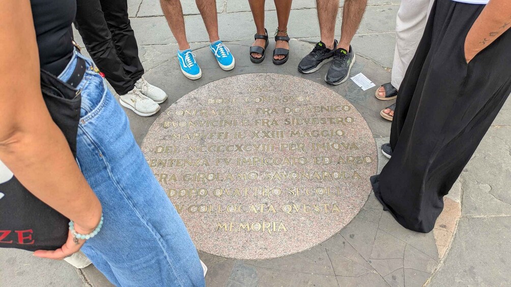 A group of people standing around a commemorative plaque on a sidewalk. 1