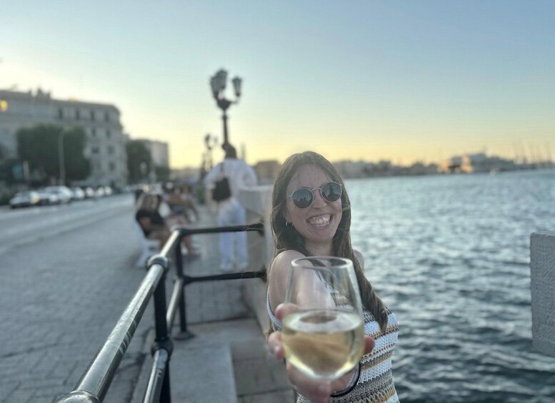 En person som håller i ett glas vitt vin, lutar sig mot ett räcke och har en vattenyta i bakgrunden. 2