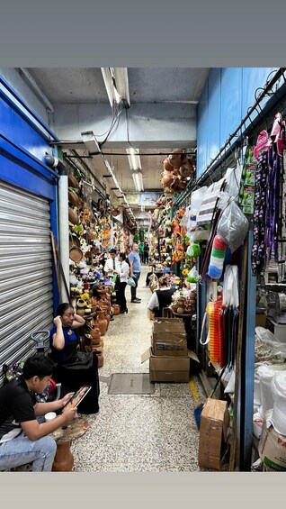 A narrow market aisle with various stalls selling pottery, textiles, and other goods. 3