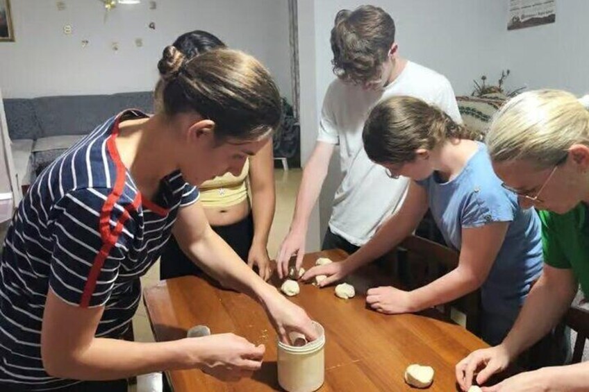 Un gruppo di persone prepara cibo, mentre una persona taglia pasta su un tavolo di legno. 3