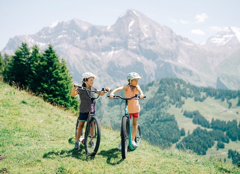 Two people on bicycles on a grassy hill with a mountainous landscape in the background. 5