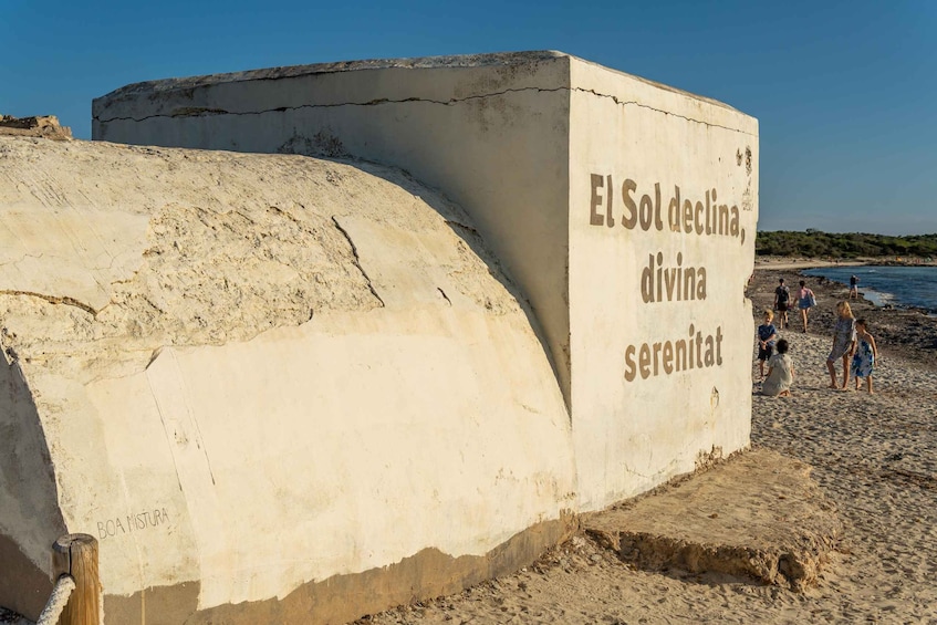 A large concrete structure with text on it, located on a sandy beach with people in the background. 3