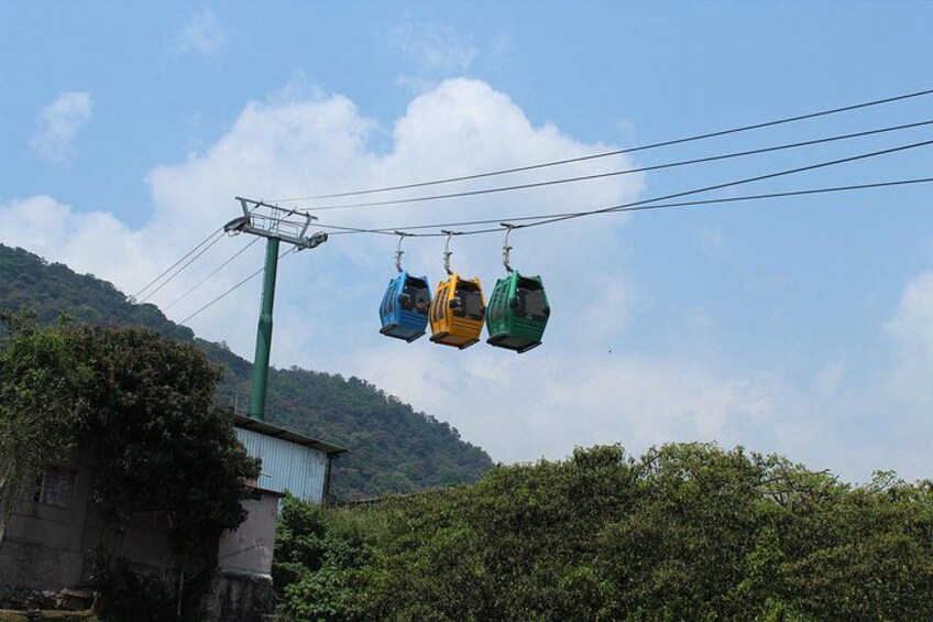 A cable car system with three cabins suspended by cables against a backdrop of a hilly landscape and a clear sky. 4
