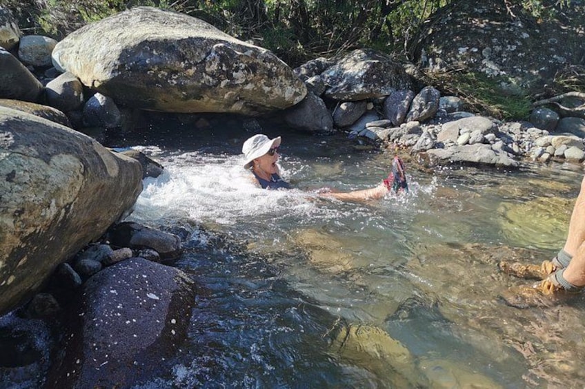 A person swimming in a clear stream surrounded by large rocks. 1