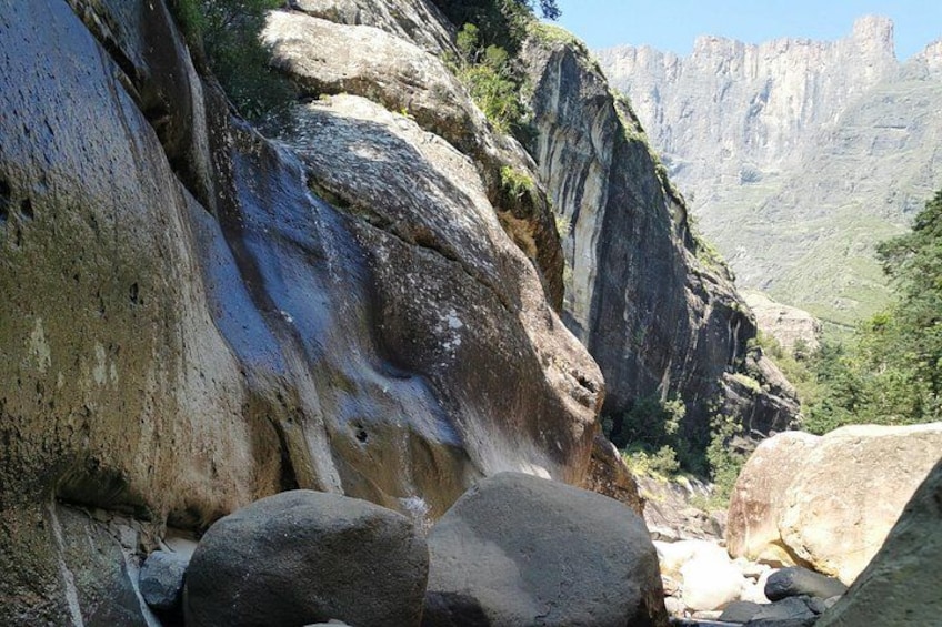 A rocky landscape with a waterfall, large boulders, and a mountainous backdrop. 5