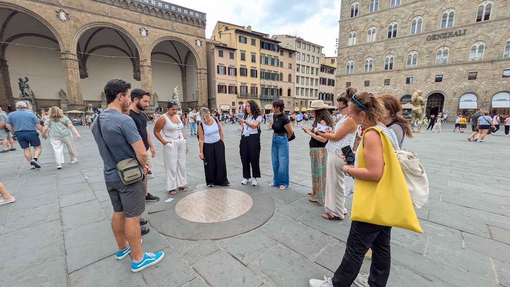 A group of people standing in a public square with historic buildings in the background. 1