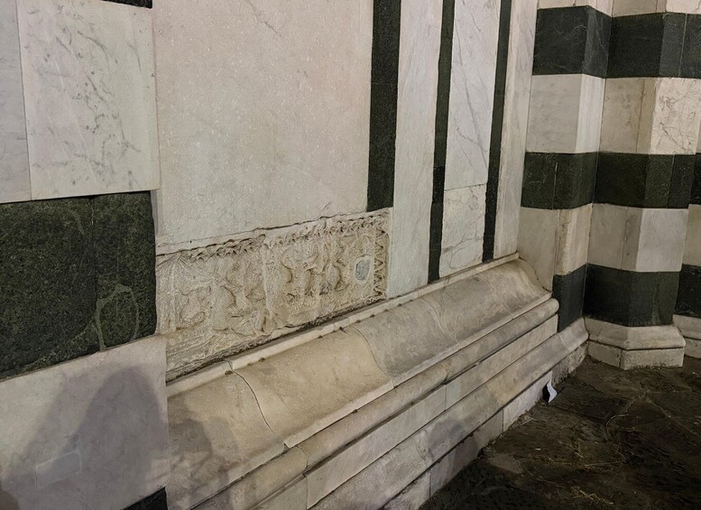 A stone wall with a relief sculpture and a corner with alternating white and dark tiles. 5