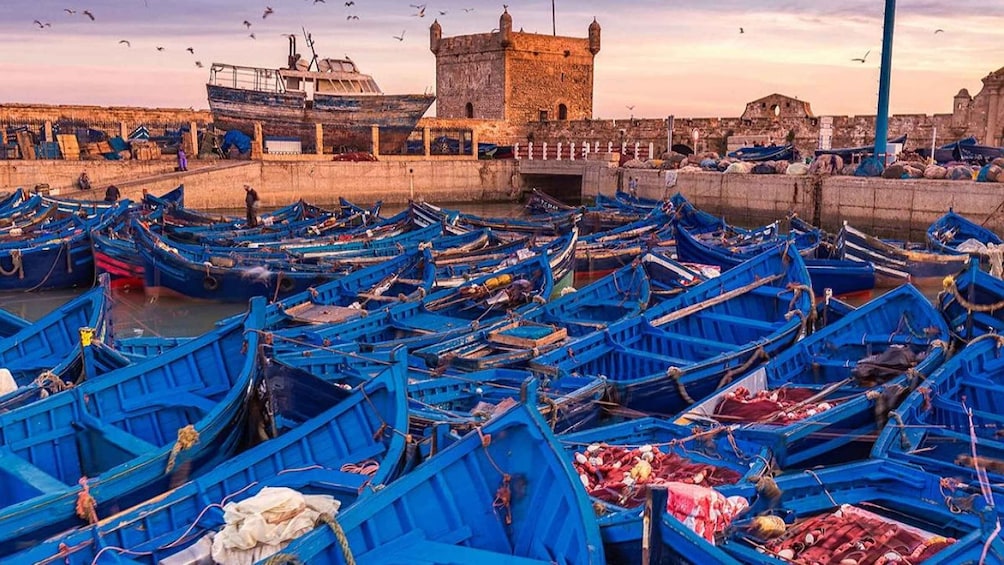 A harbor filled with blue boats, a stone tower, and a bridge. 1