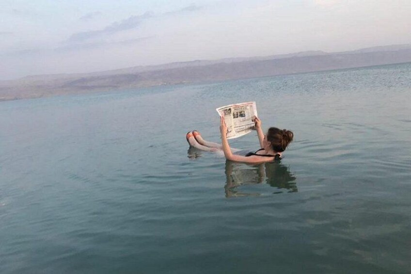 A person floating in a body of water, holding a newspaper. 1
