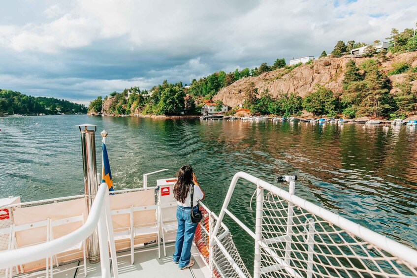 A person standing on a boat deck overlooking a calm lake with boats docked along the shore and a hilly landscape in the background. 3