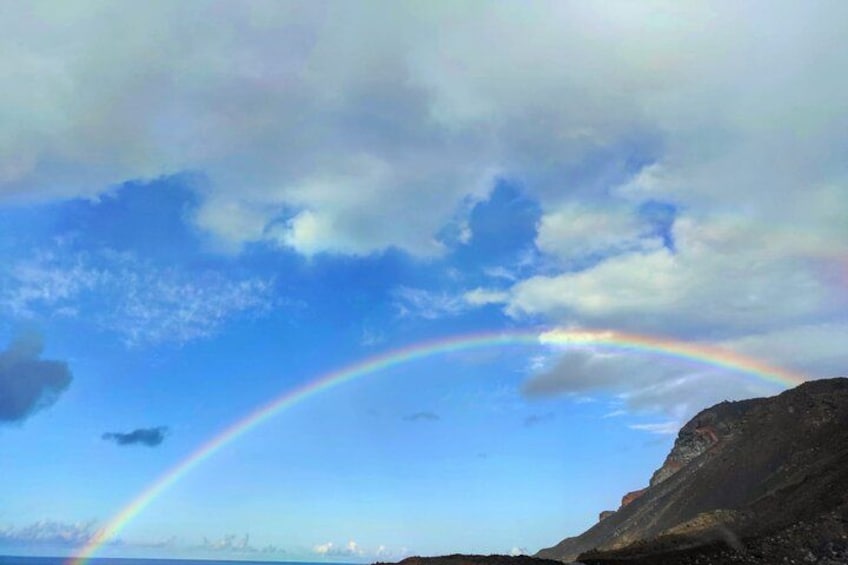 A coastal landscape with a rainbow arching over a rocky cliff. 2