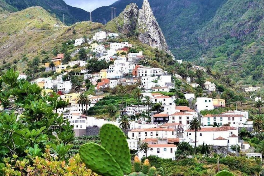 Un village côtier aux bâtiments blancs, bordé de palmiers, avec une montagne rocheuse imposante qui se dresse à l’arrière-plan. 4
