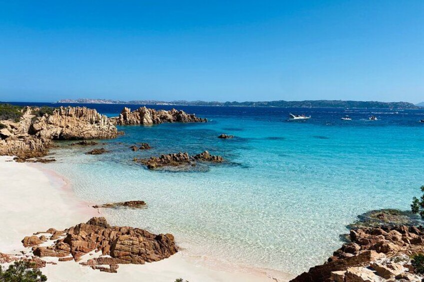 A coastal landscape with clear turquoise waters, rocky formations, and a sandy beach. 1