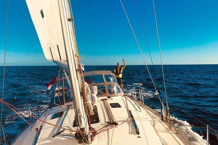 A sailboat with a person on deck, a clear blue sky, and calm sea. 3