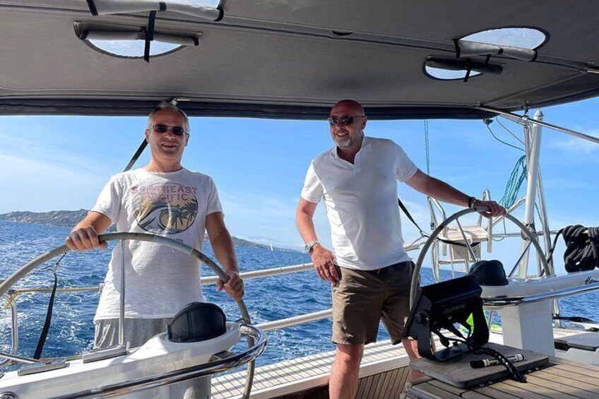 Two people on a sailboat, one steering and the other standing by. 4