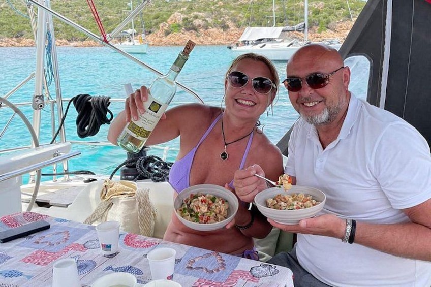 Deux personnes dînent sur un bateau, une nappe est dressée, une bouteille de vin blanc est posée sur la table, et un plat de nourriture se trouve devant elles. 2