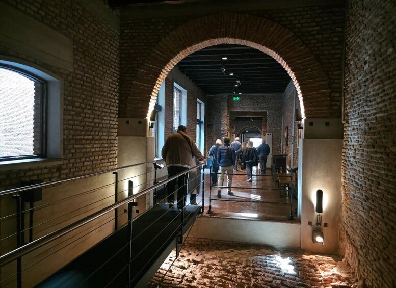 A brick-walled corridor with a staircase, people walking, and a window on the left. 3