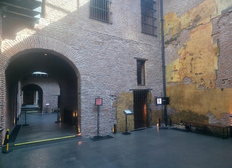 An arched brick passageway with a bench and informational signs, leading to a building with a weathered facade. 5