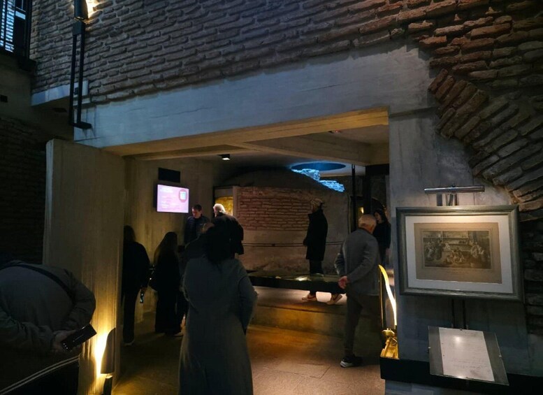 An indoor museum corridor with brick walls, a projection screen, and a framed historical painting. 4