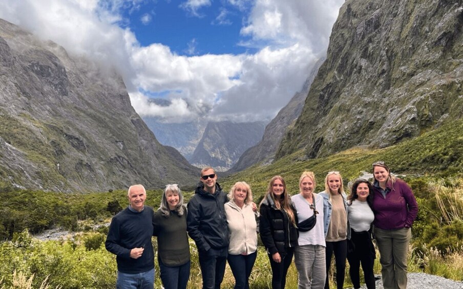 A group of people standing in a mountainous valley with rocky cliffs and greenery. 1