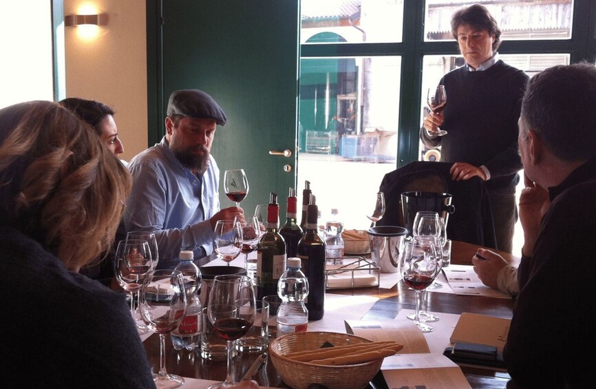 A group of people seated around a table with wine glasses and bottles, in a room with a green door and windows. 3
