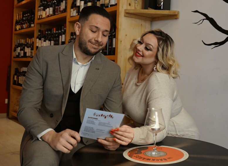 Two people seated at a table with a wine glass, surrounded by shelves of wine bottles. 4
