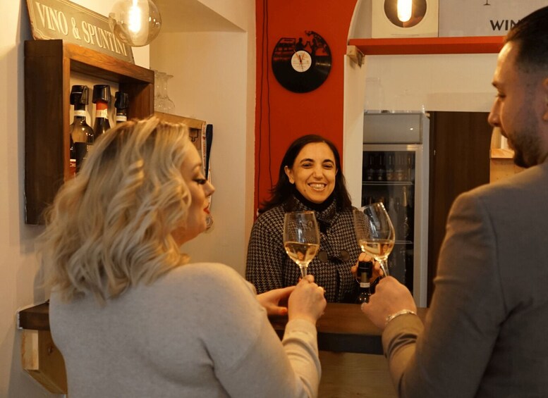 A bar with a red wall and a clock. There are bottles on shelves and people holding wine glasses. 2