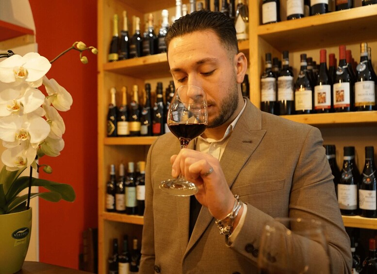 A person in a beige suit holding a wine glass, surrounded by shelves of wine bottles. 5