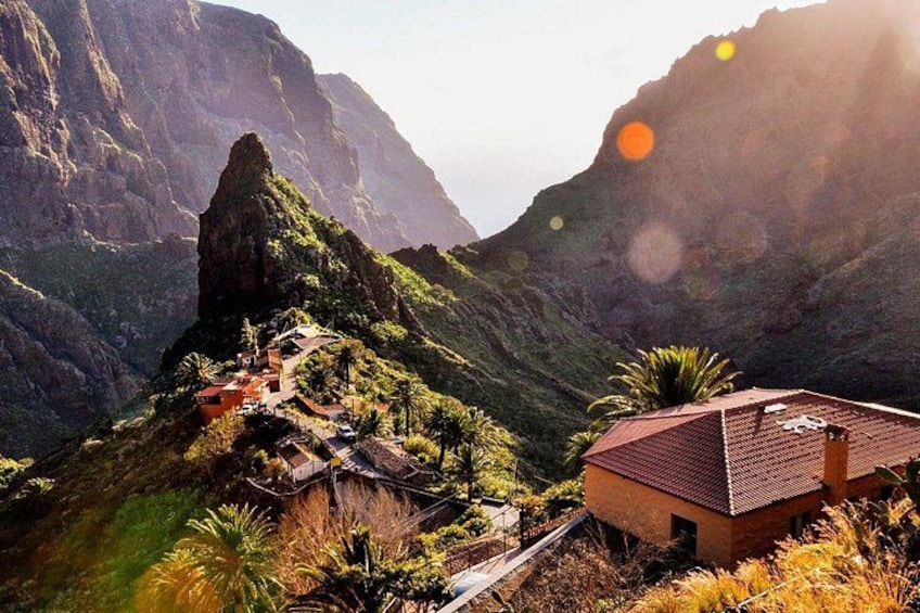 A mountainous landscape with a prominent rock formation, a small settlement with buildings, and a house with a red roof. 3