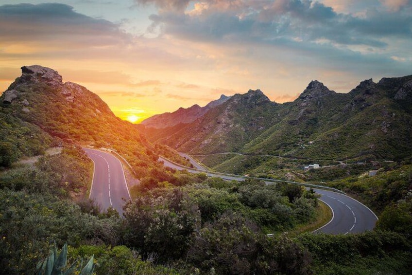A winding road through a mountainous landscape with a sunset in the background. 3
