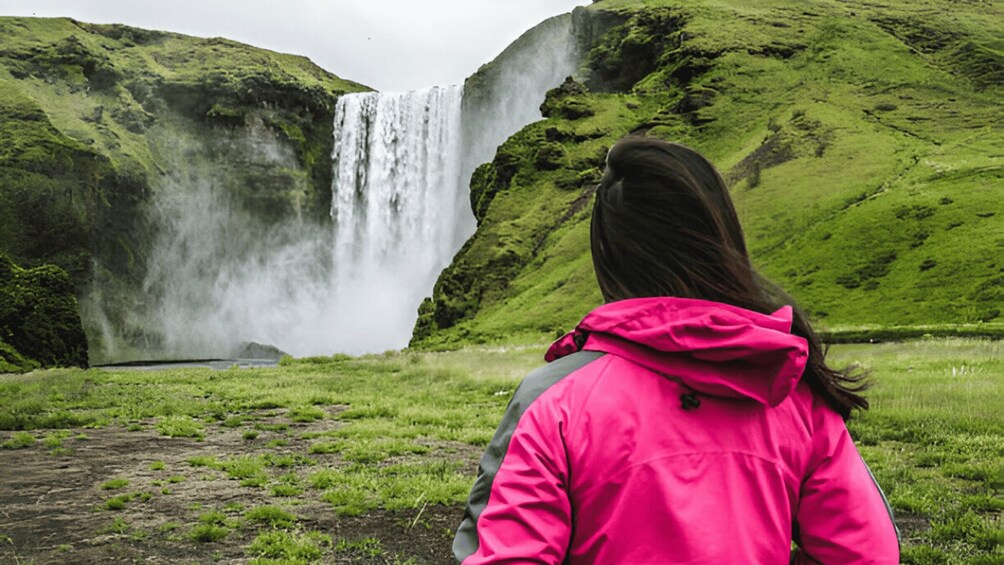 A person in a pink jacket standing in front of a waterfall. 3