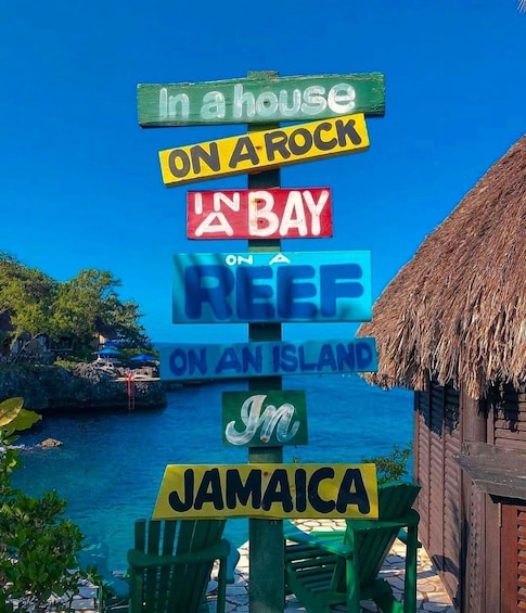 A colorful signpost with phrases like "In a house on a rock," "On a reef on an island," and "In Jamaica," set against a tropical backdrop with clear blue water and a thatched-roof hut. 5