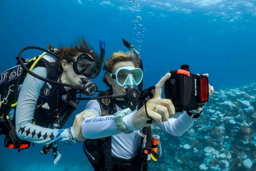 Two scuba divers taking a selfie underwater with coral formations in the background. 3