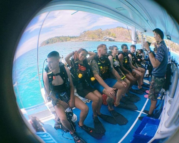 A group of people on a boat wearing diving gear, sitting on a blue deck. 1