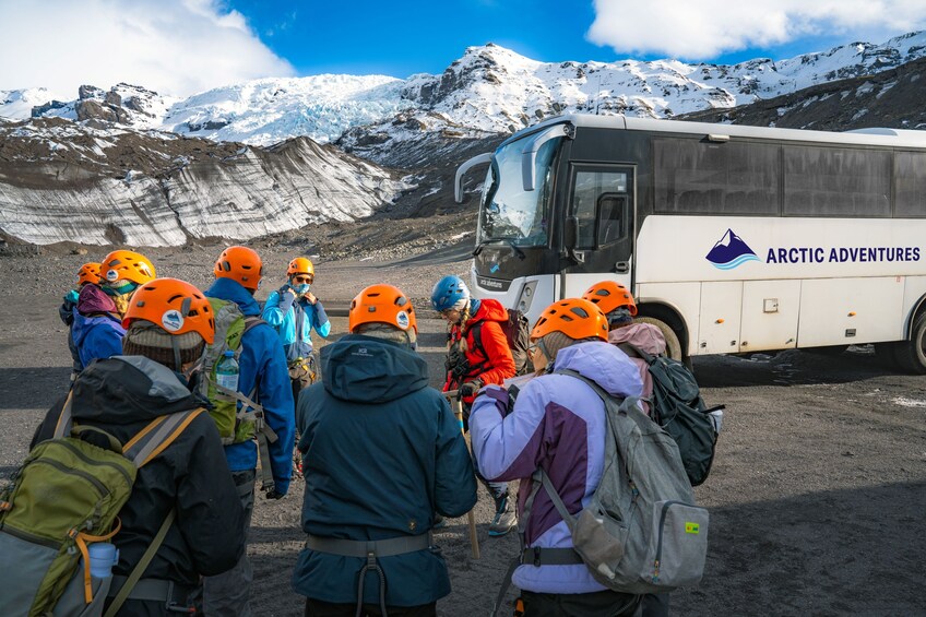 A group of people with helmets and backpacks gathered around a bus labeled 'Arctic Adventures' in a snowy mountainous area. 4