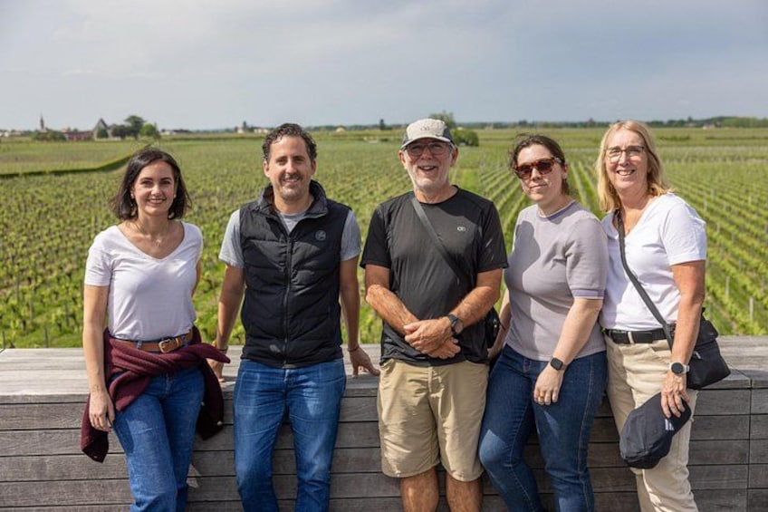 Un groupe de personnes se tient sur une plateforme en bois, avec un vignoble en arrière-plan. 2