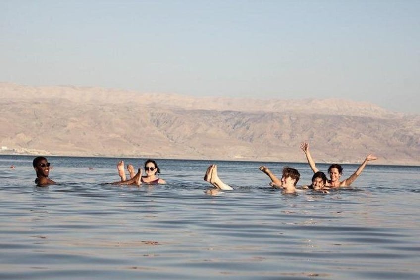 Un groupe de personnes nage dans une étendue d’eau, avec un paysage désertique en arrière-plan. 2