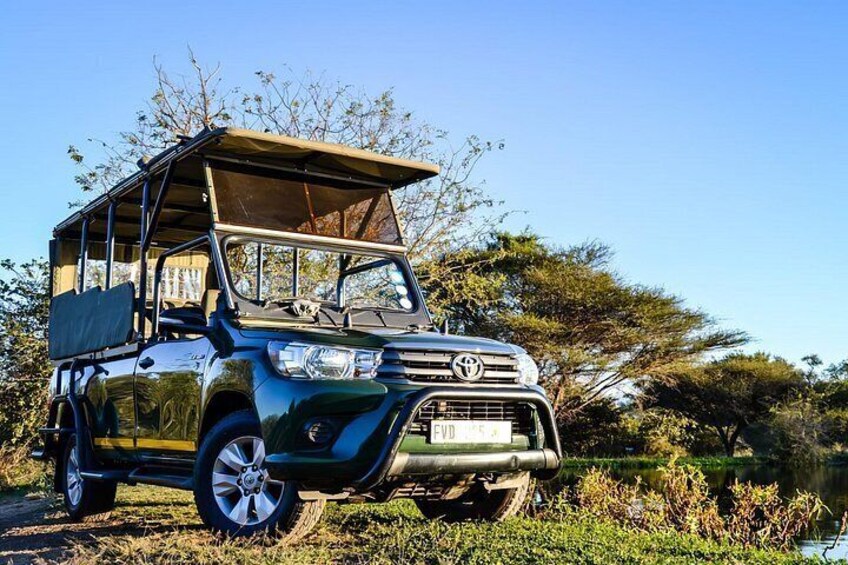 En Toyota Land Cruiser med ett öppningsbart tak, parkerad på en grusväg omgiven av grönska och träd. 1