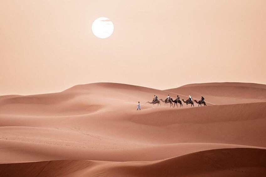 A desert landscape with sand dunes and a group of people riding camels. 1