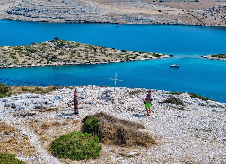 A rocky landscape with two people standing on a hill overlooking a blue body of water. 1