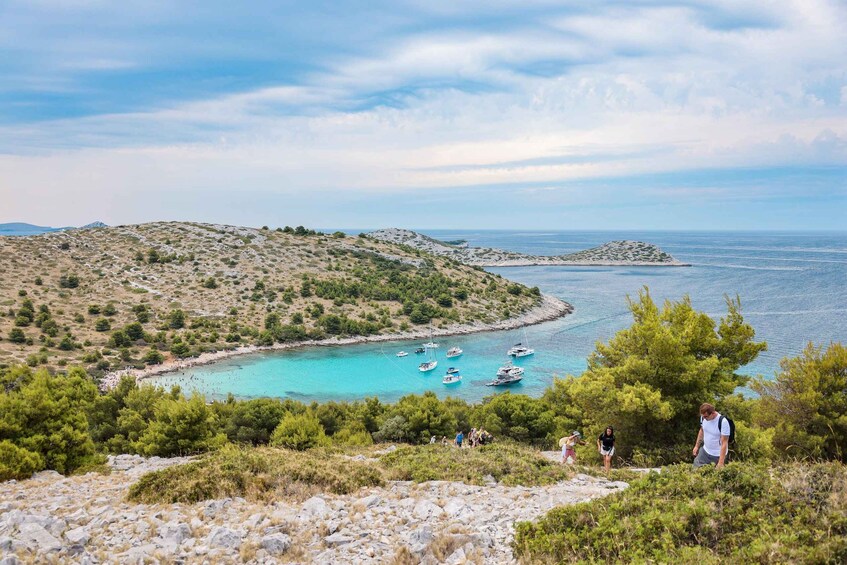 A coastal landscape with boats anchored near a turquoise bay, surrounded by rocky hills and sparse vegetation. 3