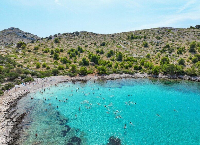 A turquoise coastal area with people swimming and sunbathing on the beach. 4