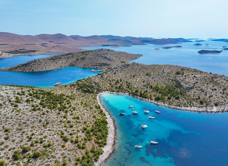 A coastal landscape with clear blue waters, boats anchored near the shore, and hilly terrain in the background. 5