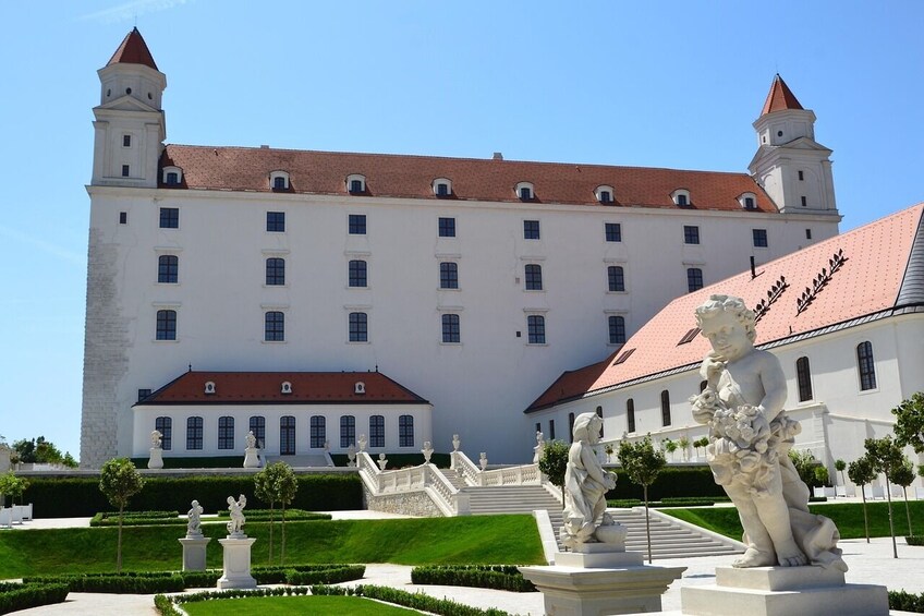 Un grand bâtiment blanc, doté d’un toit rouge et de deux tours, entouré d’un jardin bien entretenu et agrémenté de statues. 3